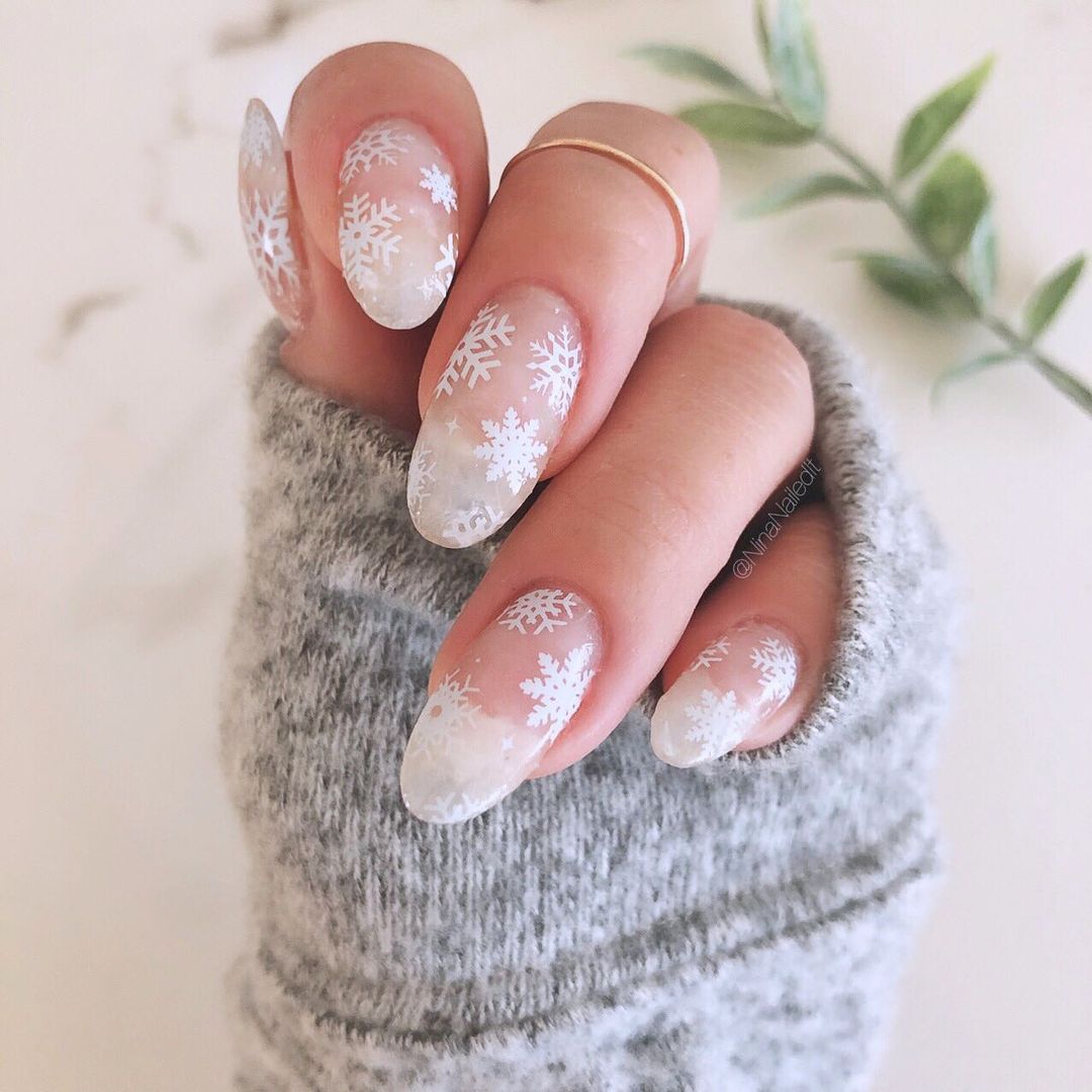 Transparent frosted nails with white snowflake designs.