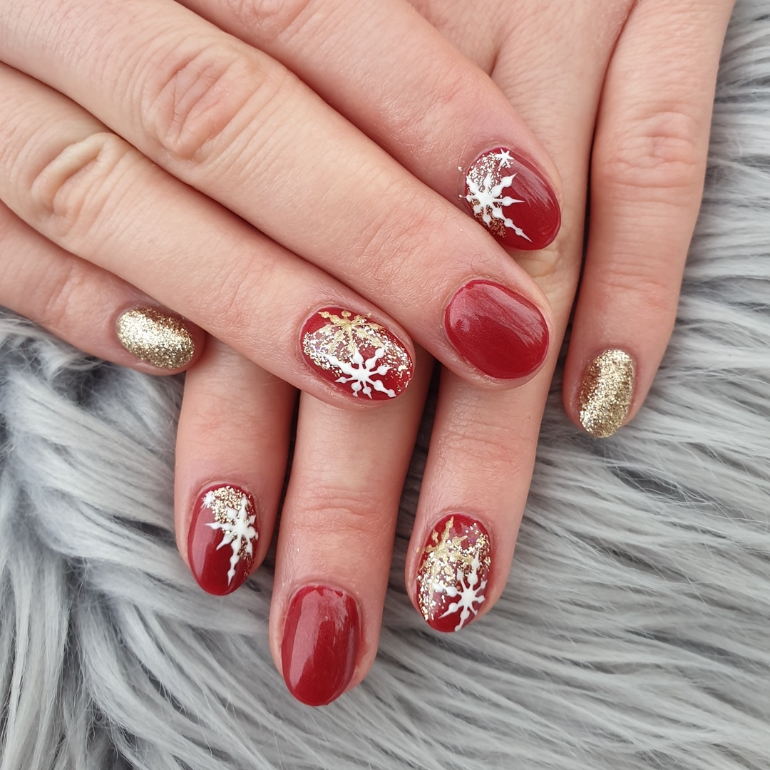 Red nails with gold glitter snowflake designs.