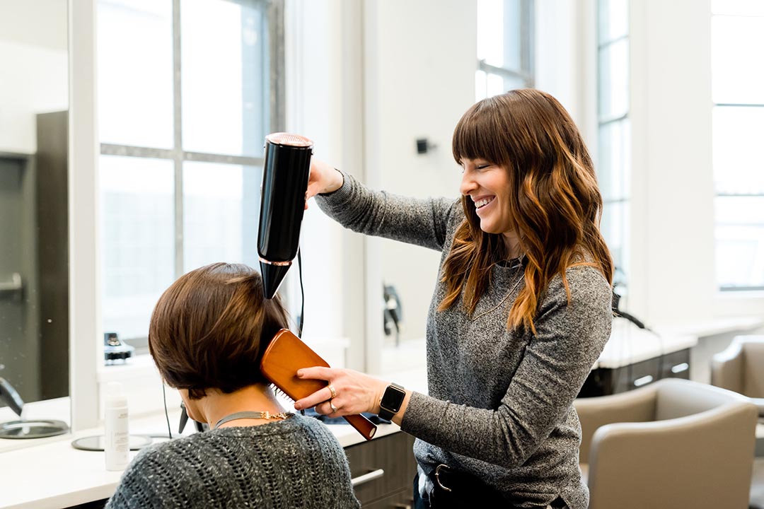 A stylist blowdrying her client's hair.
